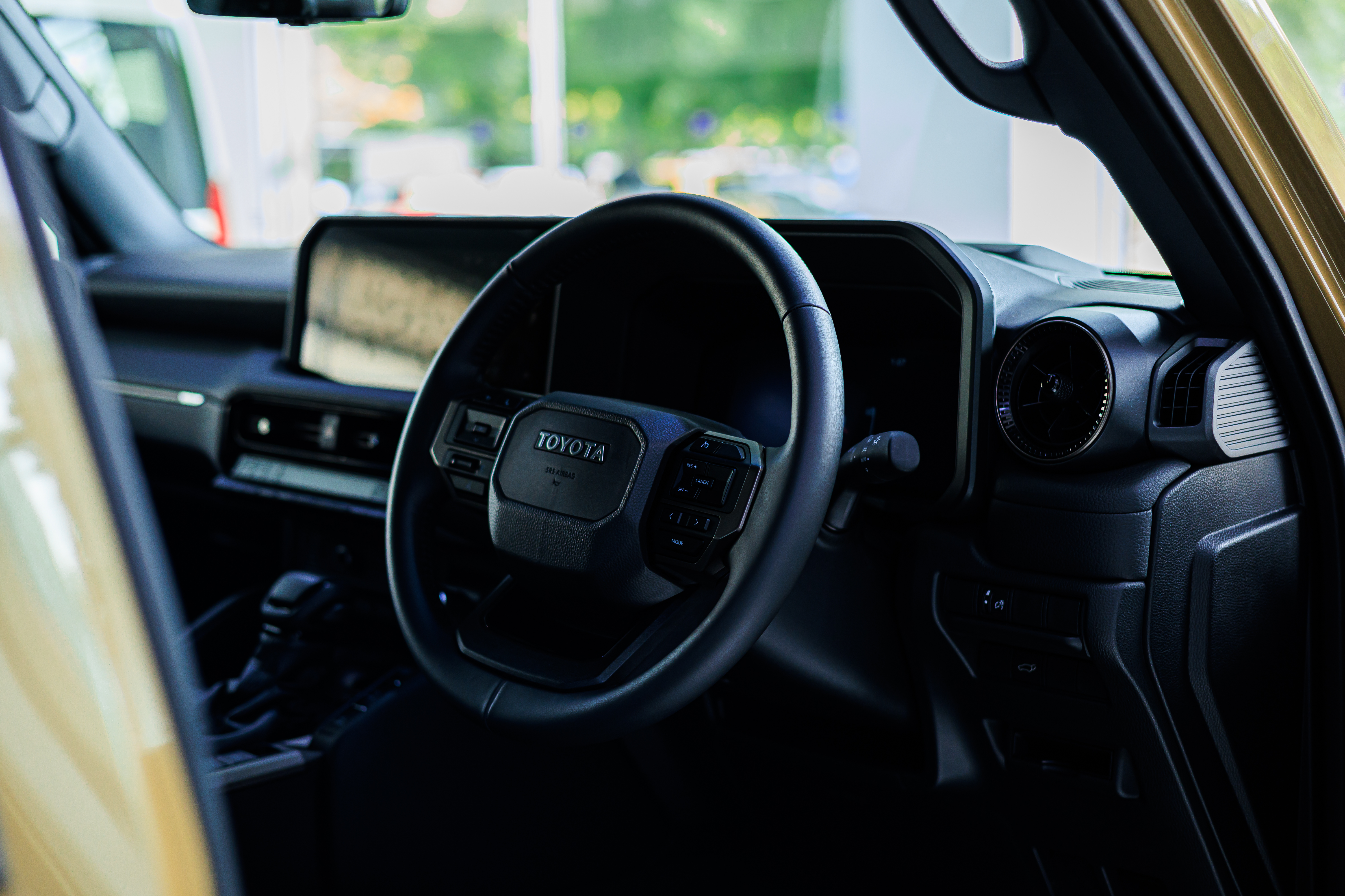 Interior view of a modern Toyota dashboard featuring a leather-wrapped steering wheel and digital display.